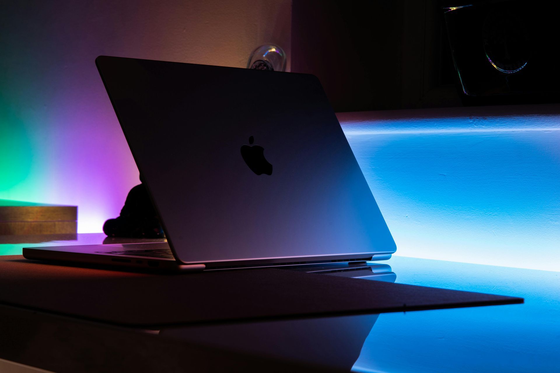 Apple laptop on a desk with colorful purple and blue LED lighting in a dark room
