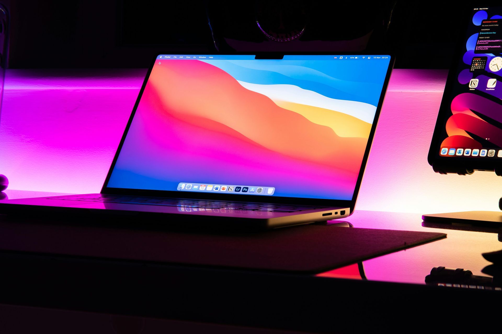 Laptop on a desk with a bright pink-and-blue display in a neon-lit room