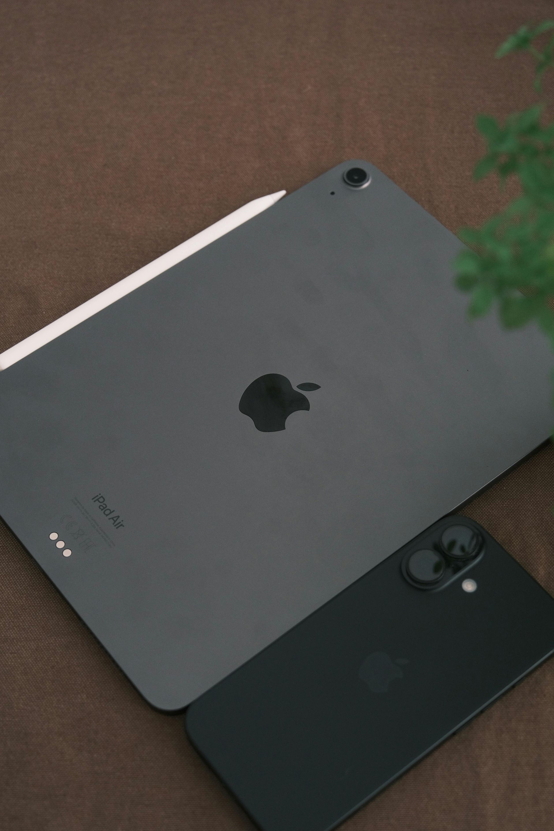 Two iPads, one silver and one black, lying on a brown surface.