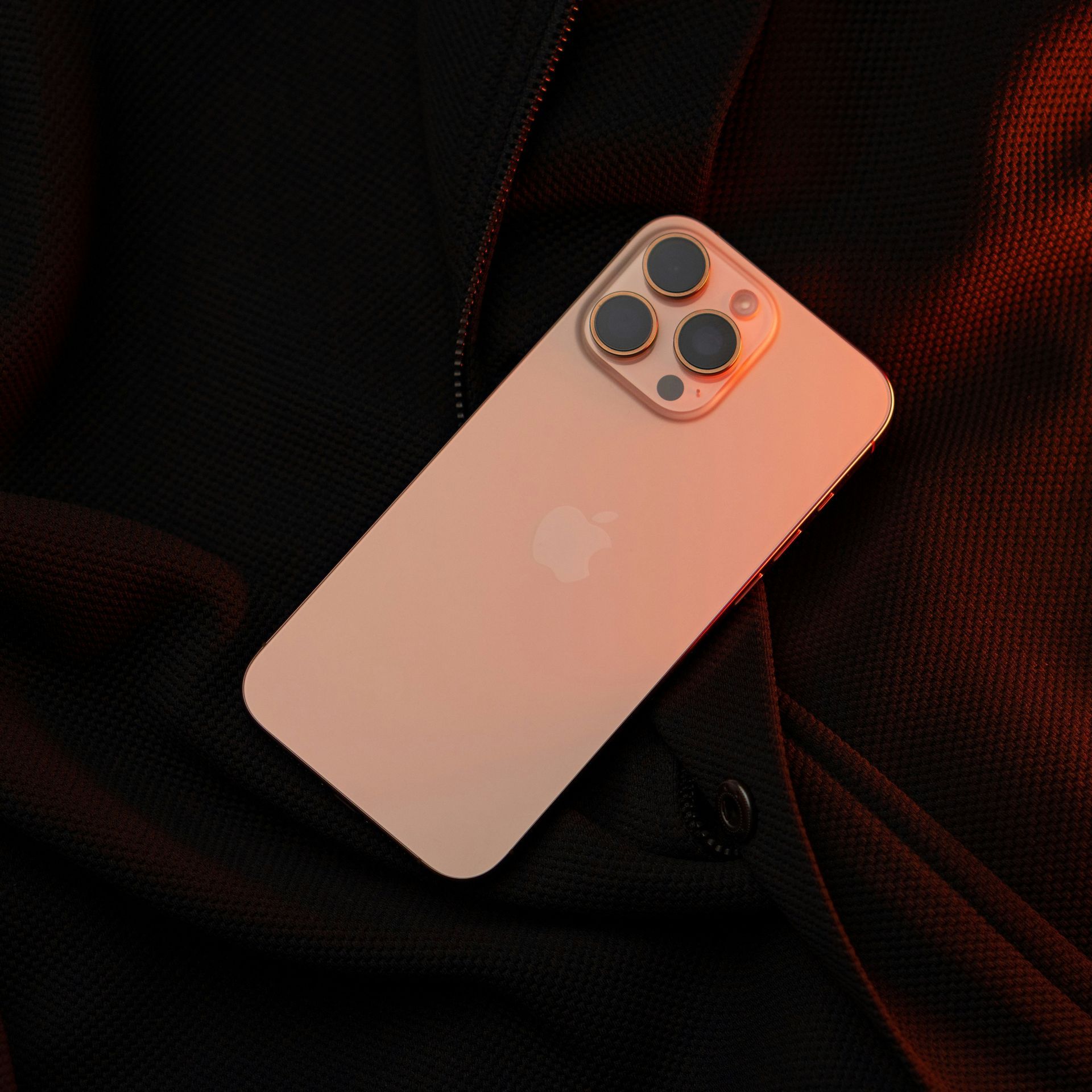 Rose gold iPhone with triple cameras lying on dark textured fabric.
