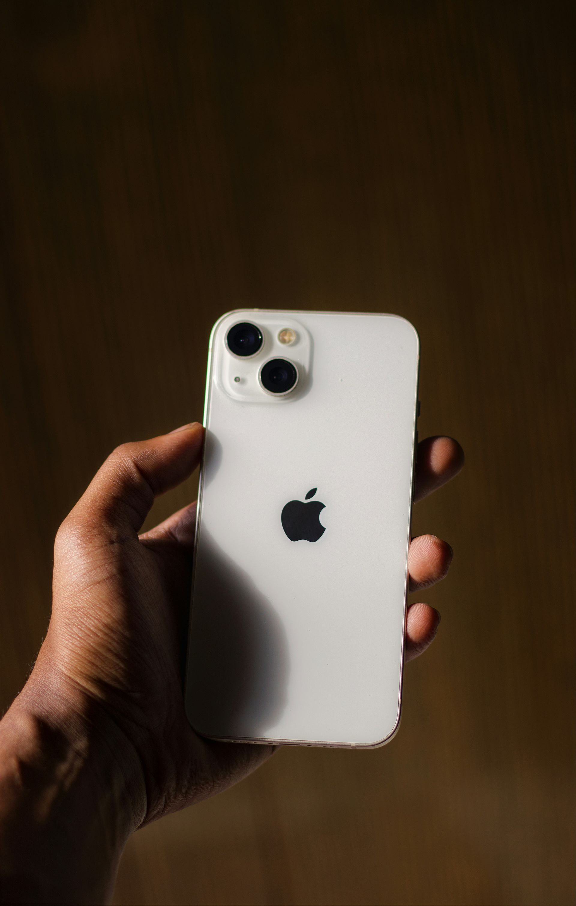 Hand holding a white iPhone with triple cameras against a dark background