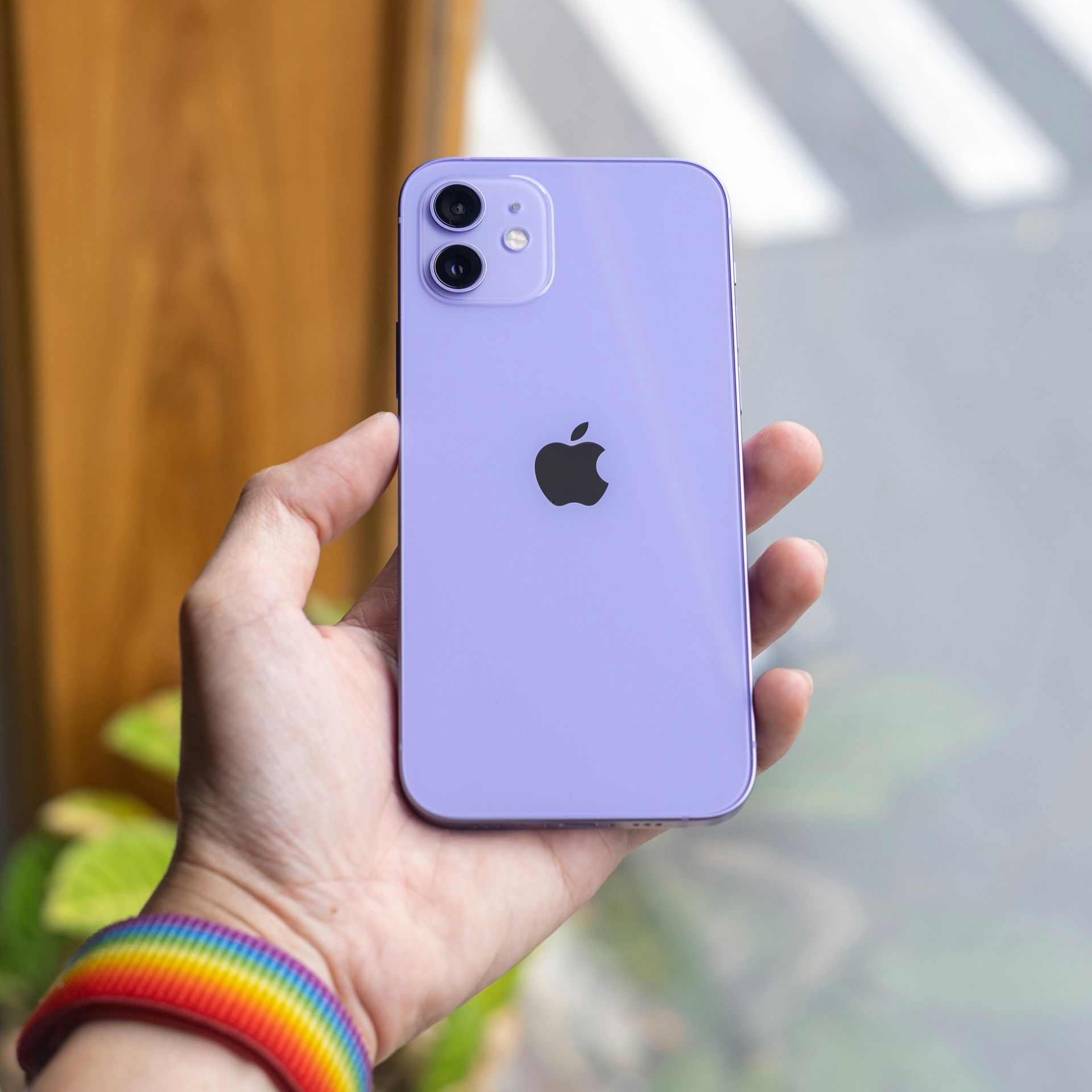 Hand holding a lavender iPhone with black Apple logo and dual cameras
