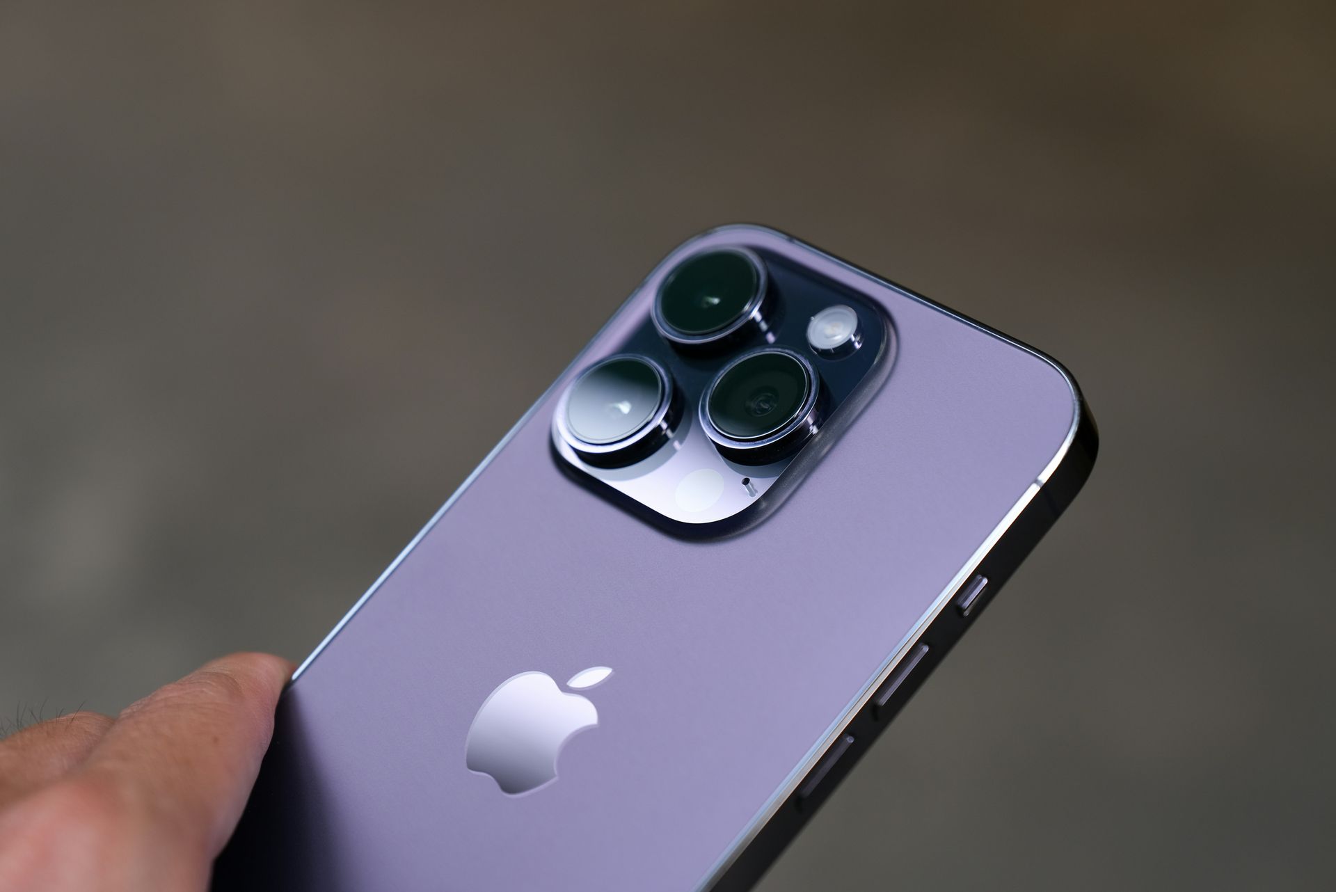 Purple iPhone with triple rear cameras held in a hand against a blurred background