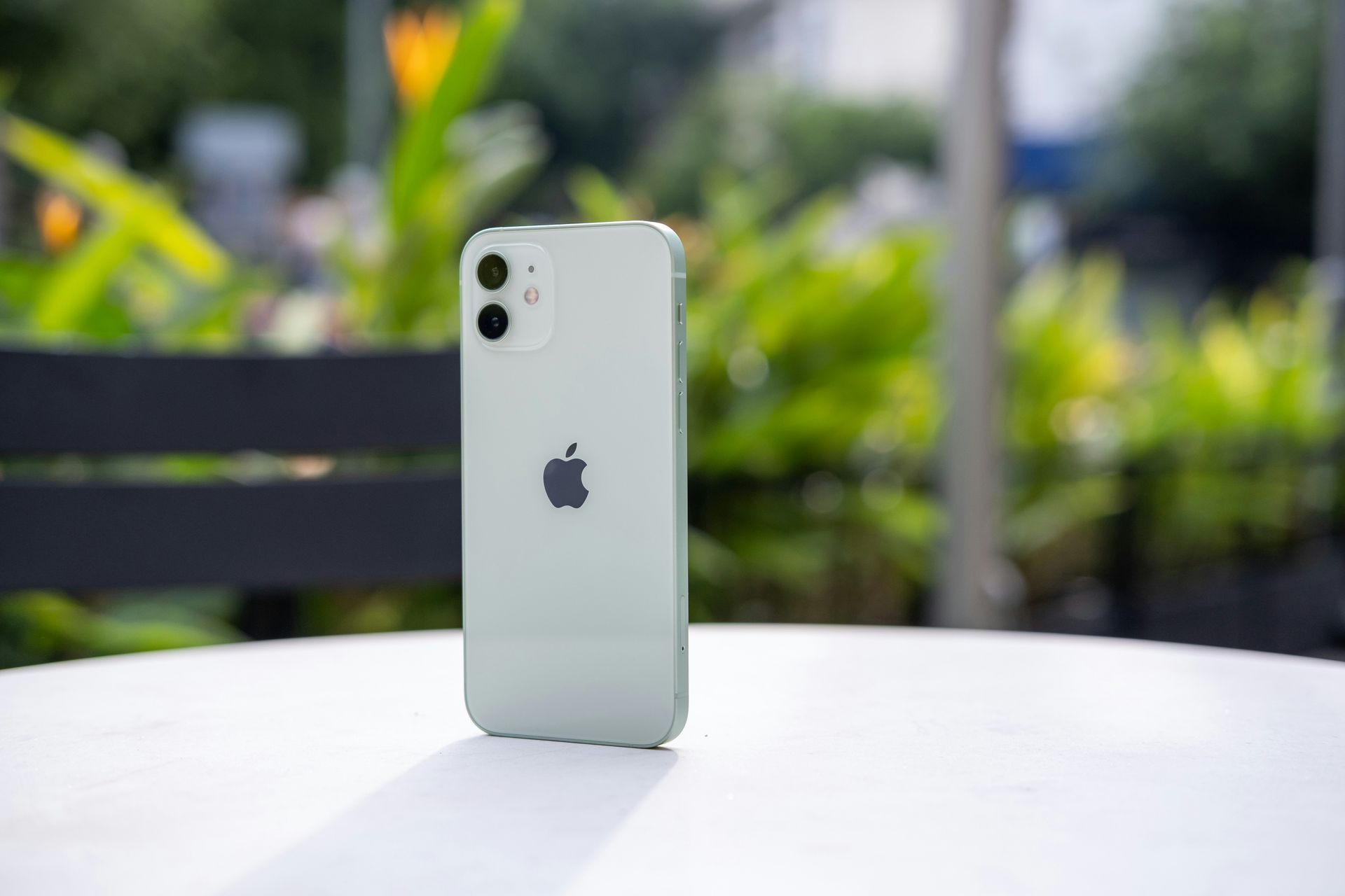 Silver iPhone standing on a white table with a blurred green outdoor background