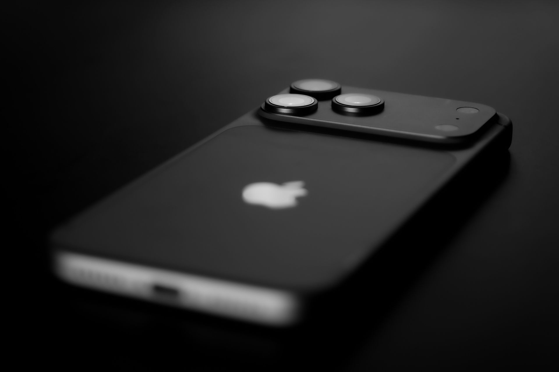 Black iPhone with triple camera lenses on a dark background
