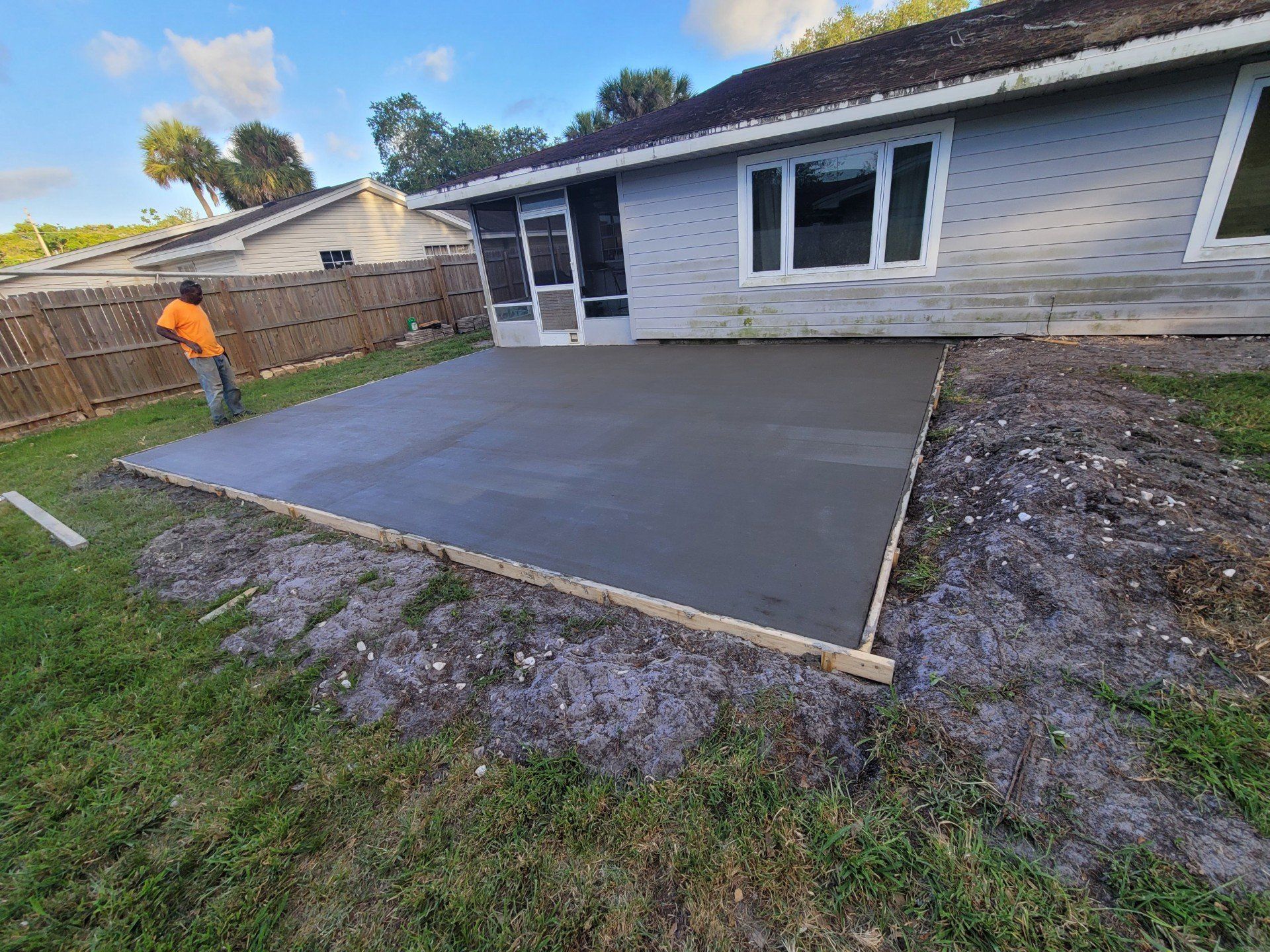 A man is working on a concrete patio in front of a house.