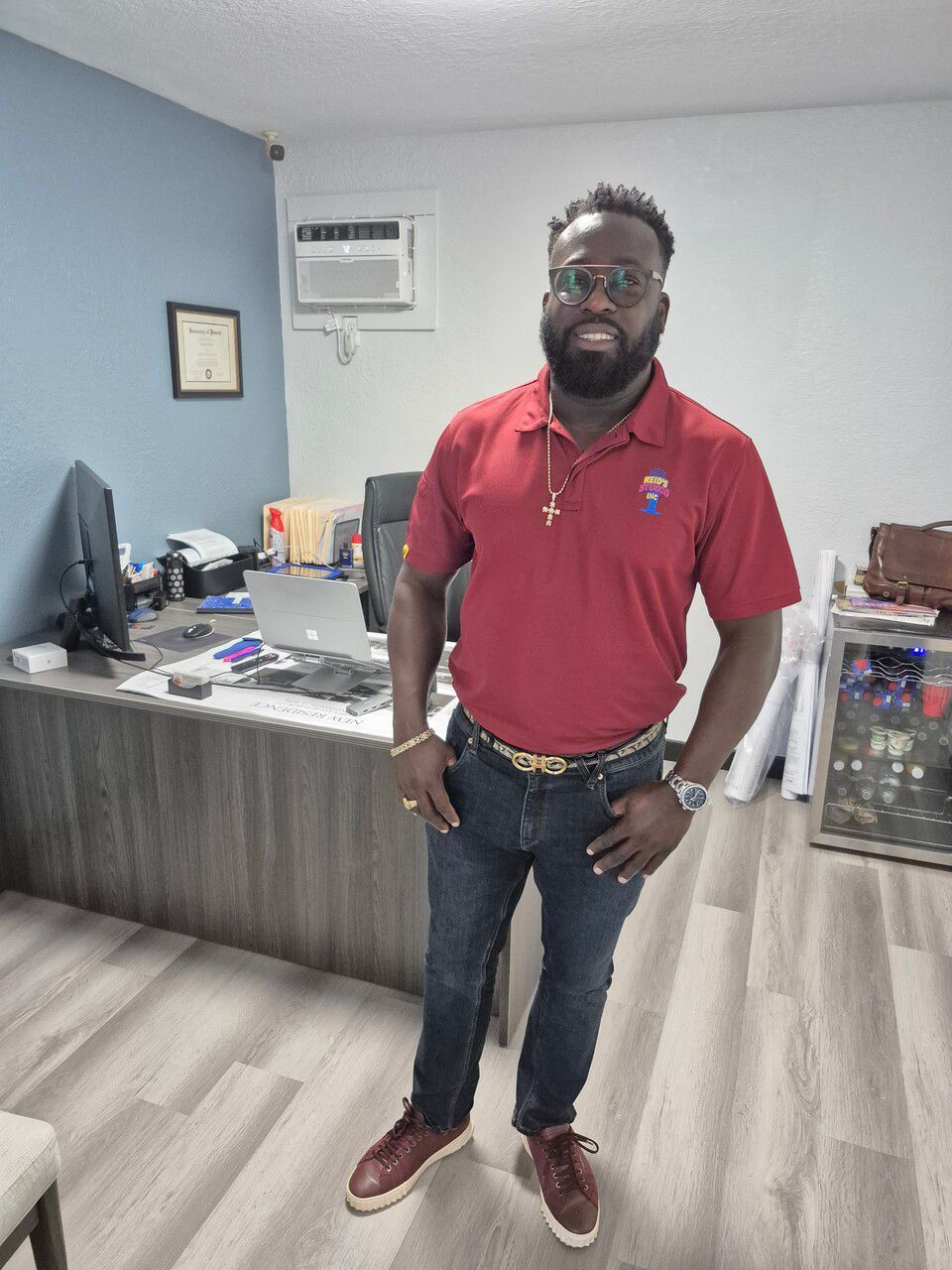 A man in a red shirt is standing in a room with his hands in his pockets.