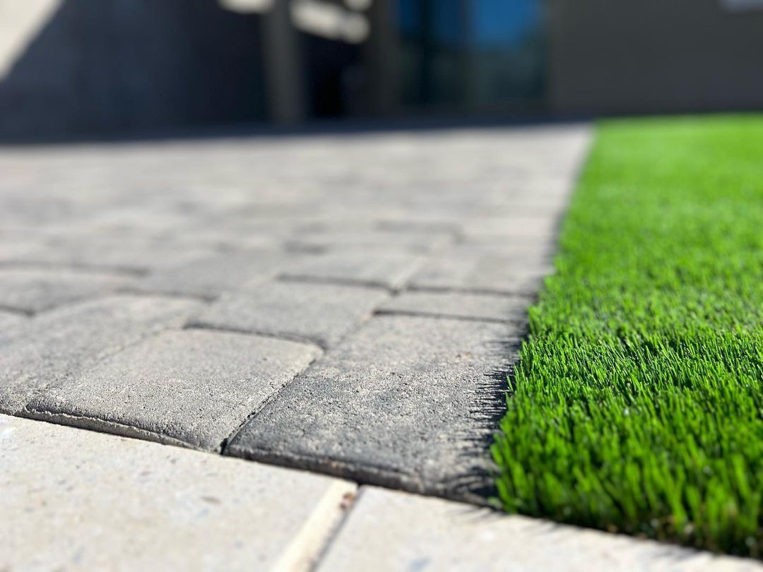 A close up of a brick walkway next to a patch of artificial grass.