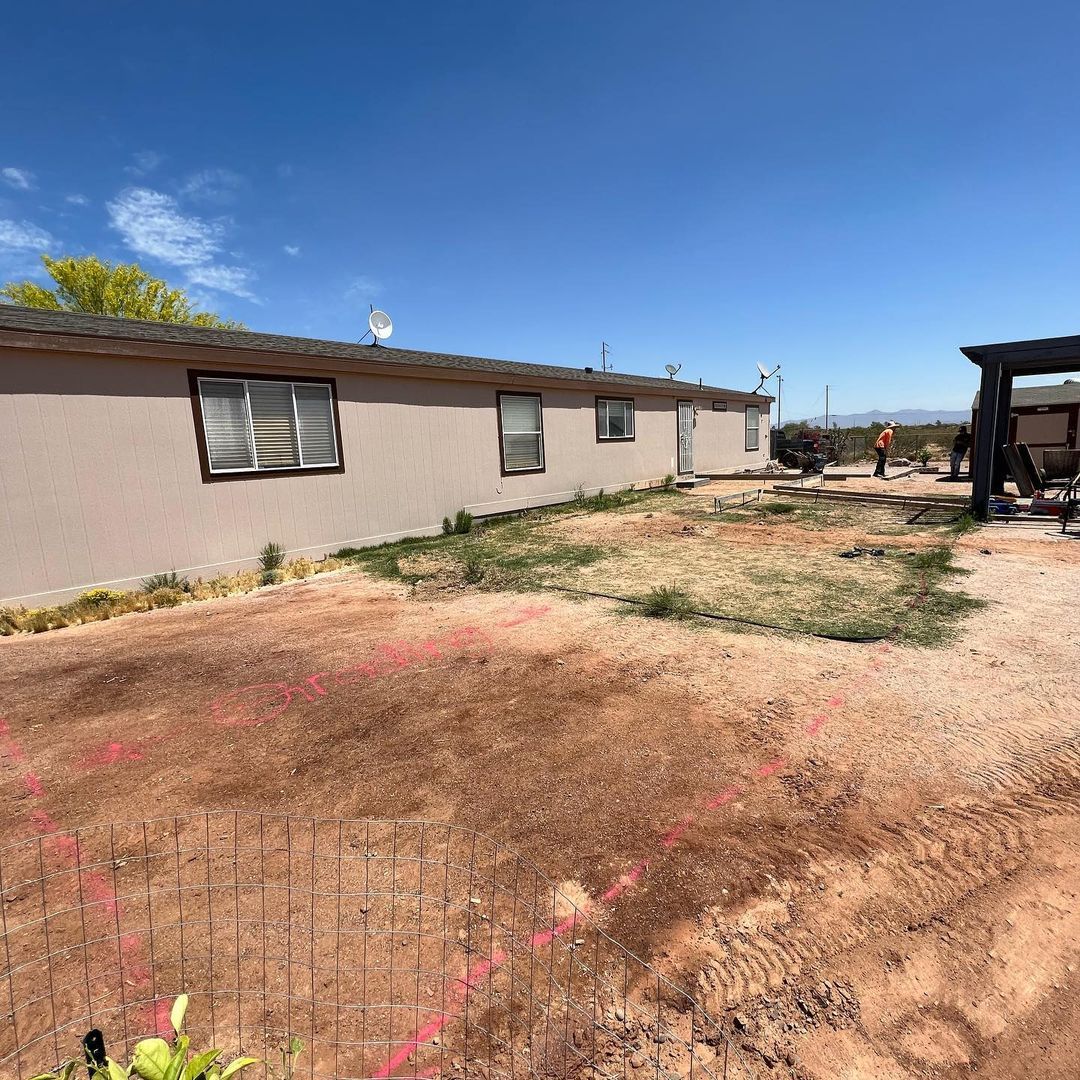 A house with a lot of windows is sitting in the middle of a dirt field.