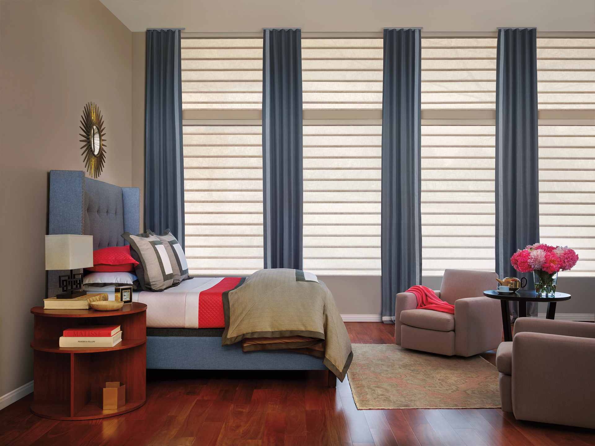 Bedroom with bed, armchairs, and windows with blue curtains and light blinds.