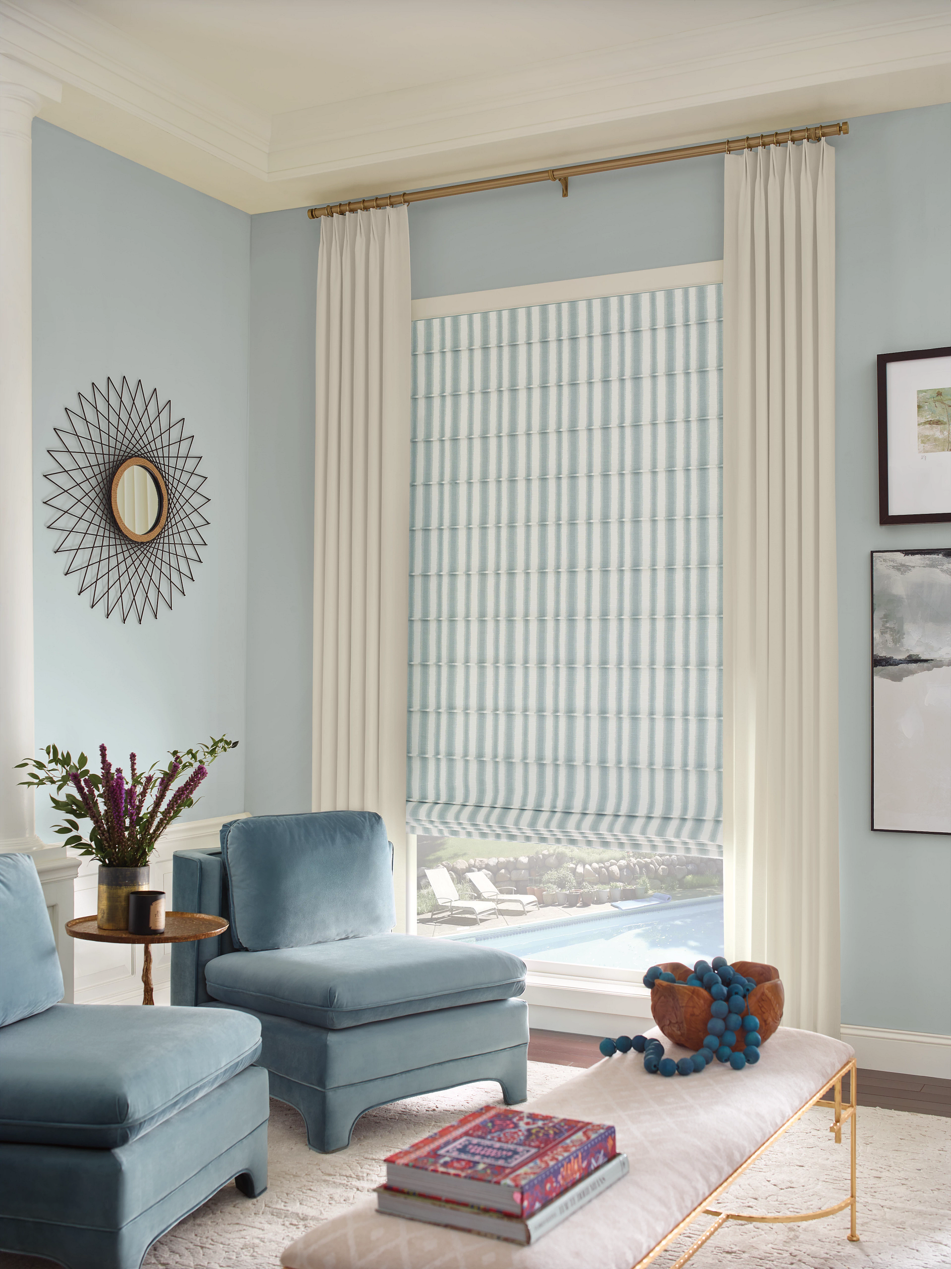 Living room with light blue walls, two blue chairs, a bench, and a window with striped shade.