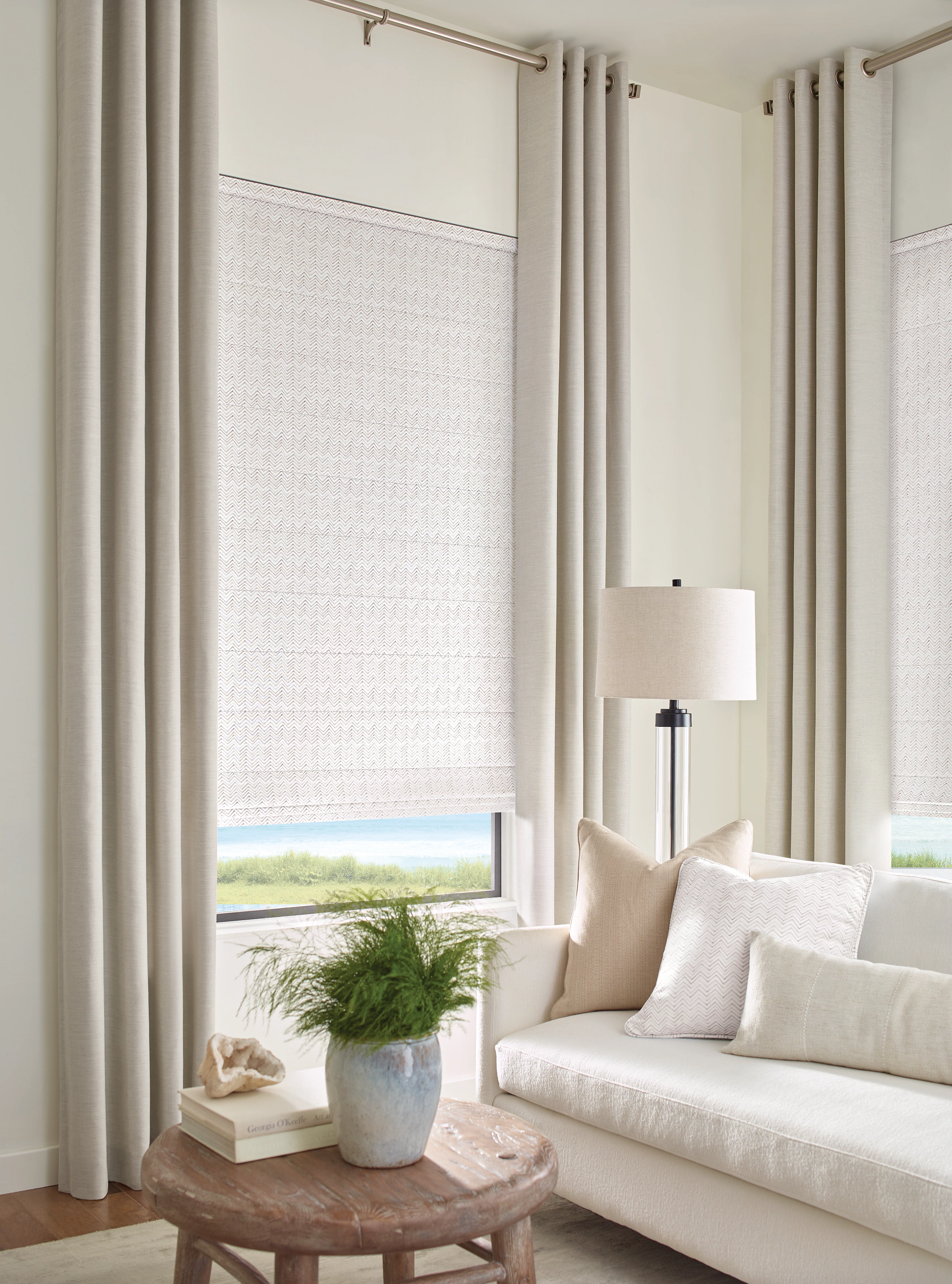 Living room with neutral curtains, a window with a patterned shade, and a light-colored couch.