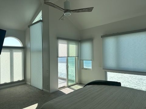 Bright bedroom with large windows, ceiling fan, and view of a balcony and ocean