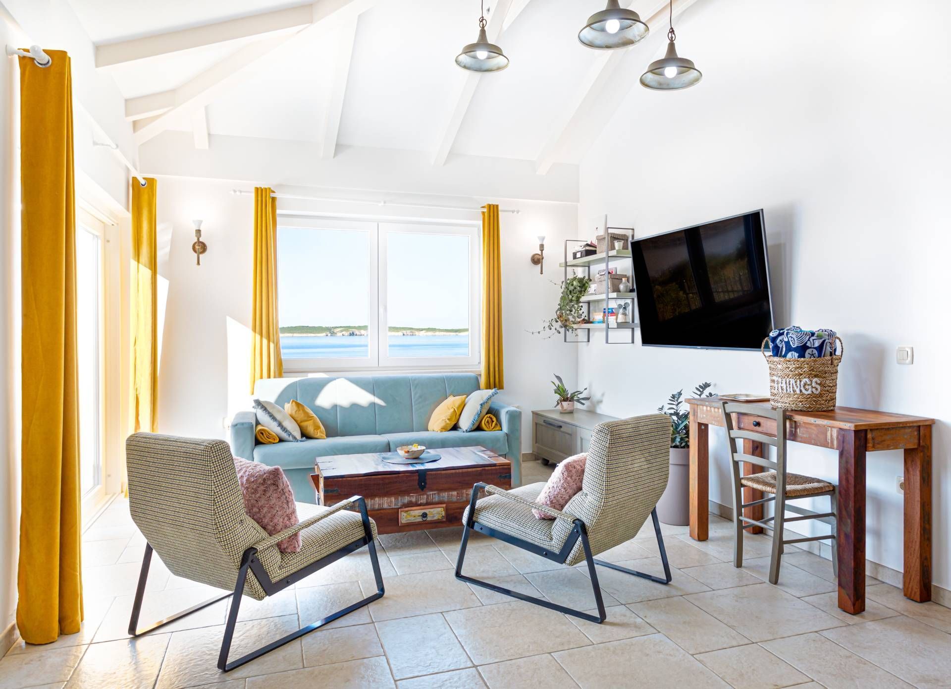 Bright living room with blue sofa, two armchairs, a TV, and yellow curtains.