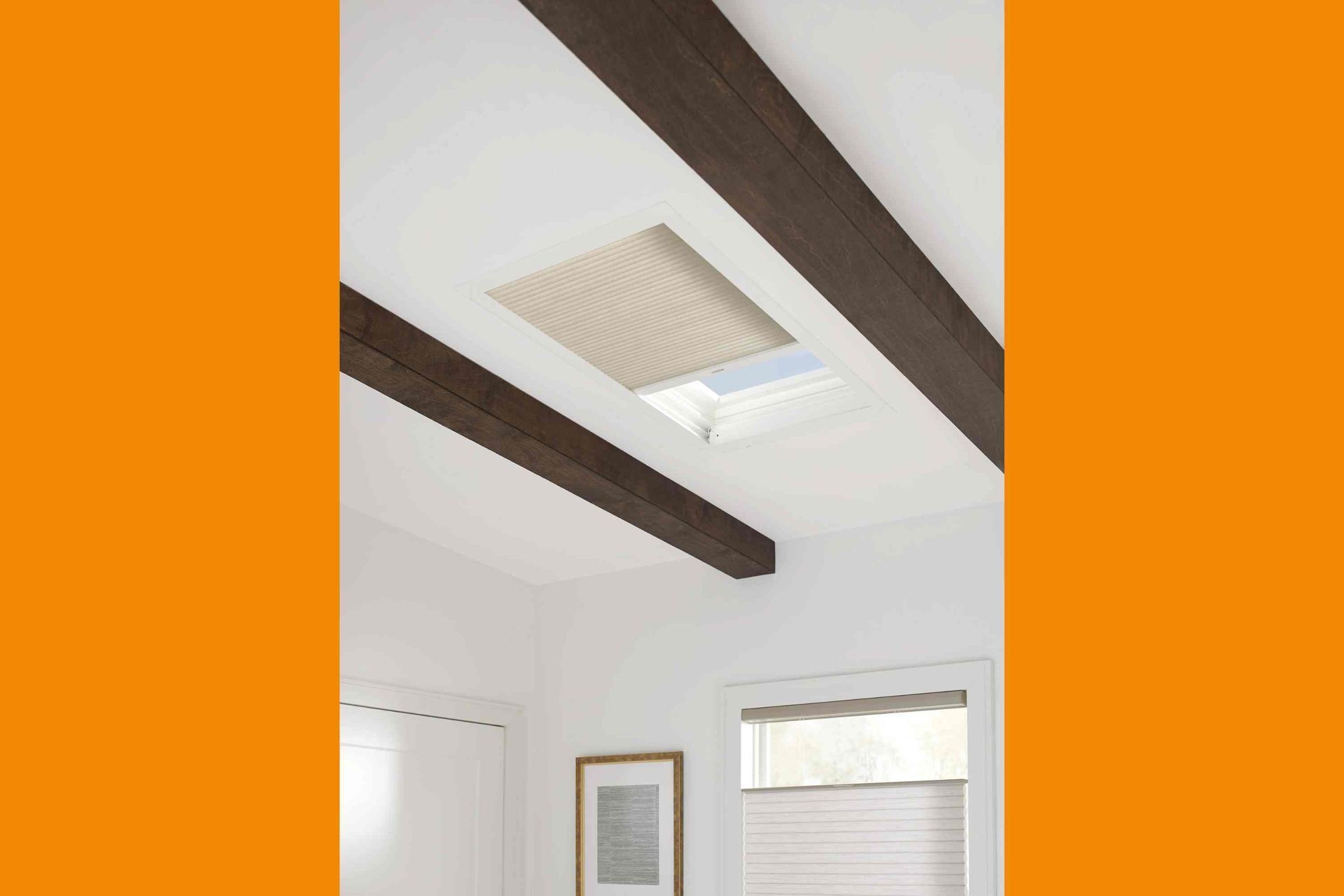 Skylight with beige honeycomb shade, framed by dark brown beams on a white ceiling.
