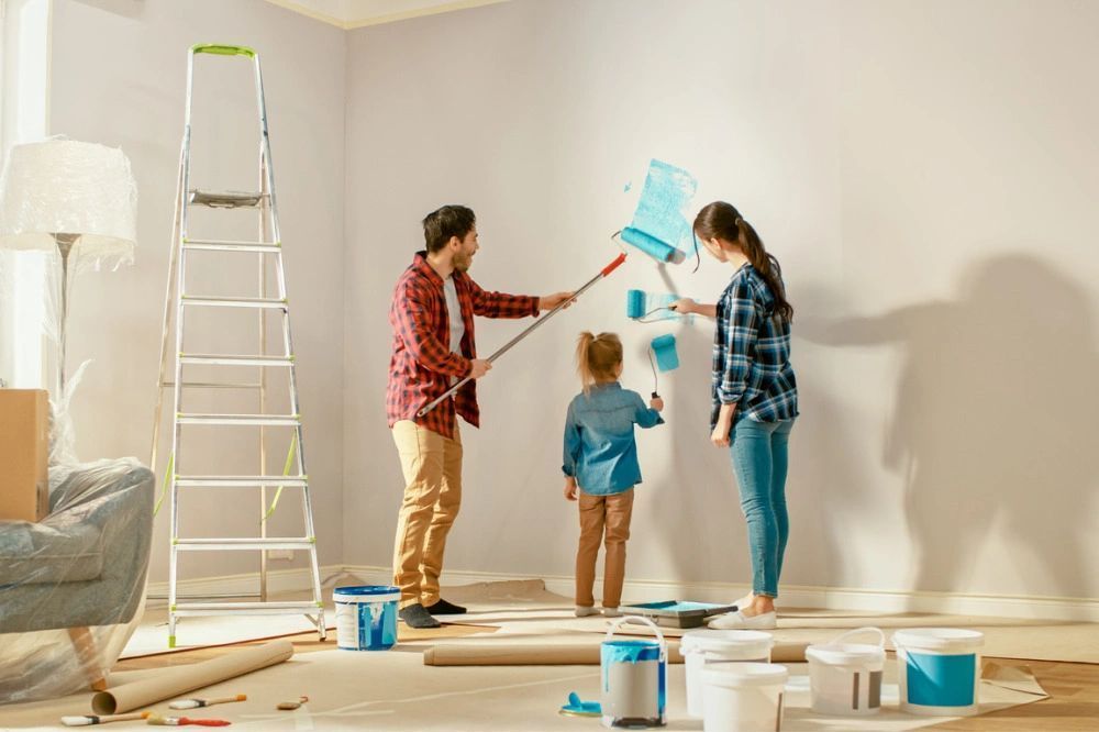 A family is painting a wall together in a living room.