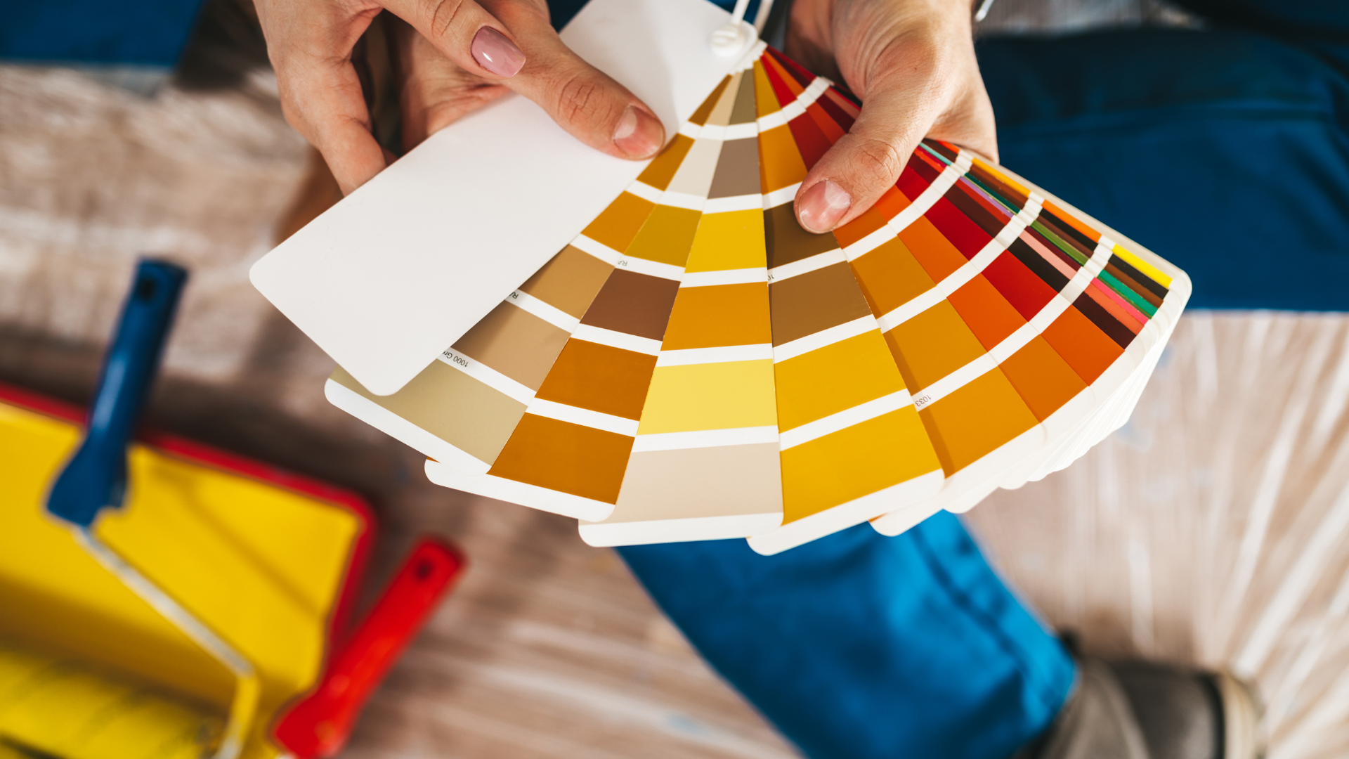 Hands holding a fan of paint swatches over a workspace with tools and fabric