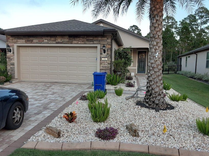 Suburban house with stone front, garage, desert landscaping, and a blue recycling bin by the driveway