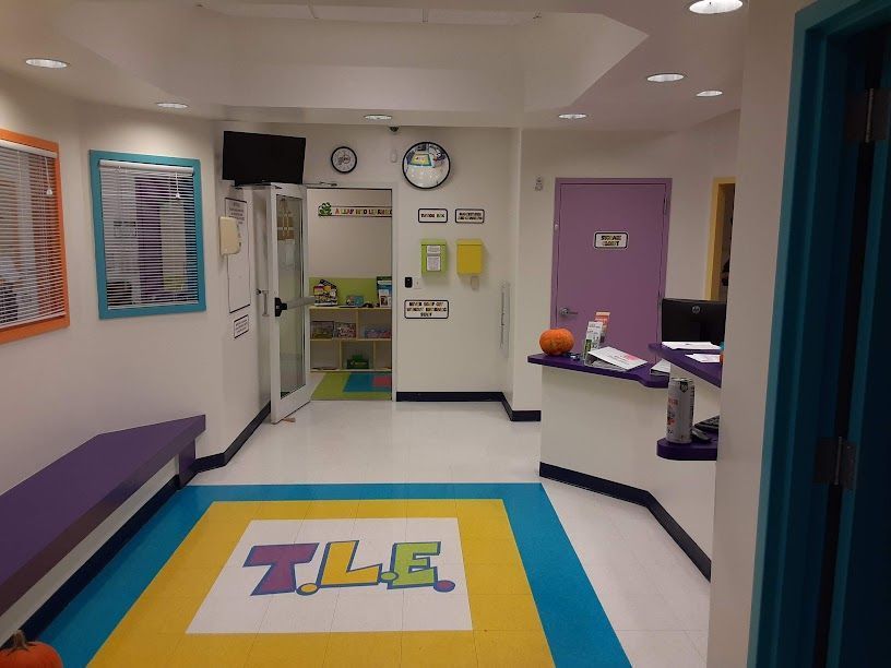 Colorful clinic waiting room with purple bench, yellow rug, open door, and reception desk.