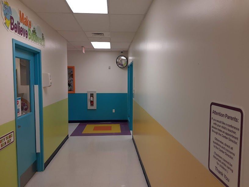 Bright hallway with teal and white walls, colorful floor border, and a classroom door on the left.