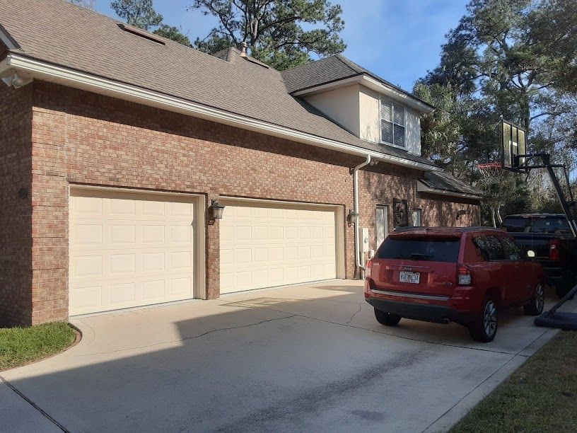 Brick suburban house with two beige garage doors and a red SUV parked in the driveway