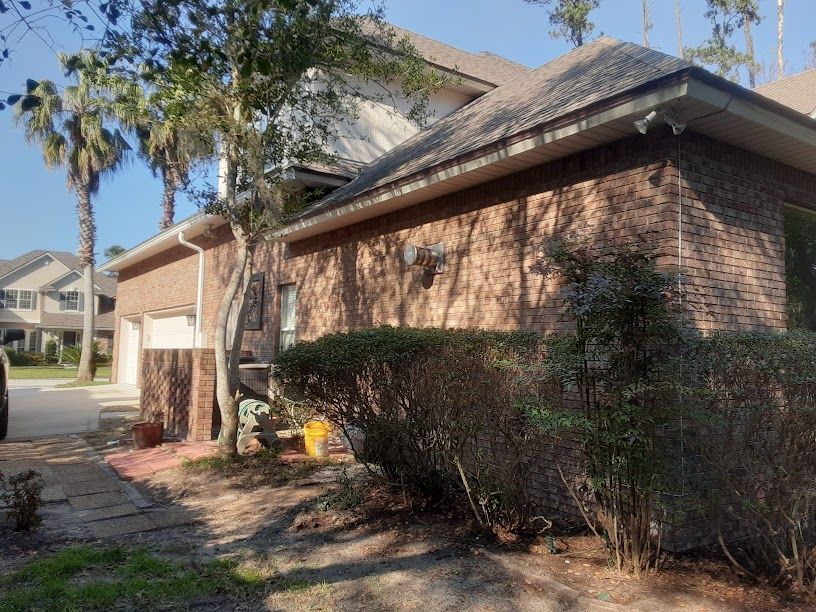 Brick suburban house with trimmed hedges, driveway, and palm trees in front yard