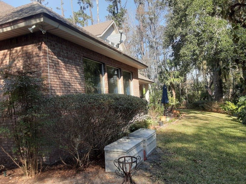 Brick house beside a grassy yard with trees and bushes in sunlight