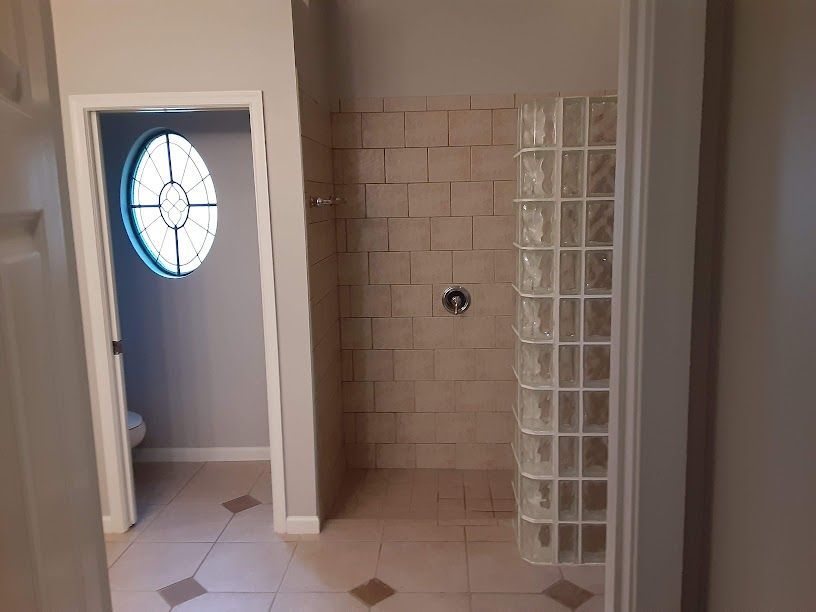 Empty tiled bathroom with a shower alcove, glass-block wall, and open doorway with round window.