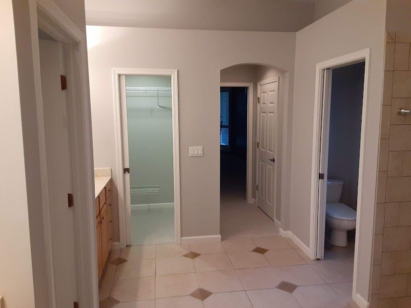 Bathroom with tiled floor, vanity on left, shower and toilet, and a hallway visible through open doorways.