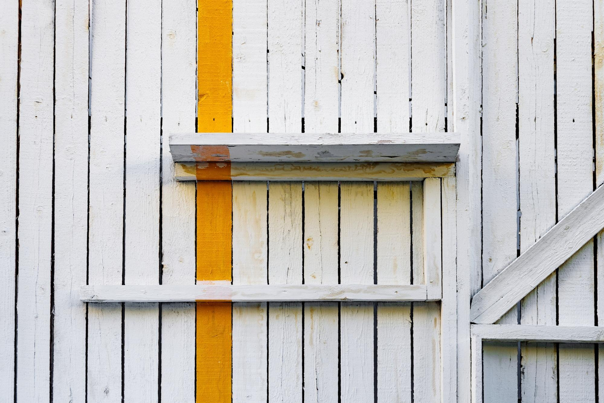 White wooden wall with two small shelves and a vertical yellow stripe painted down the center