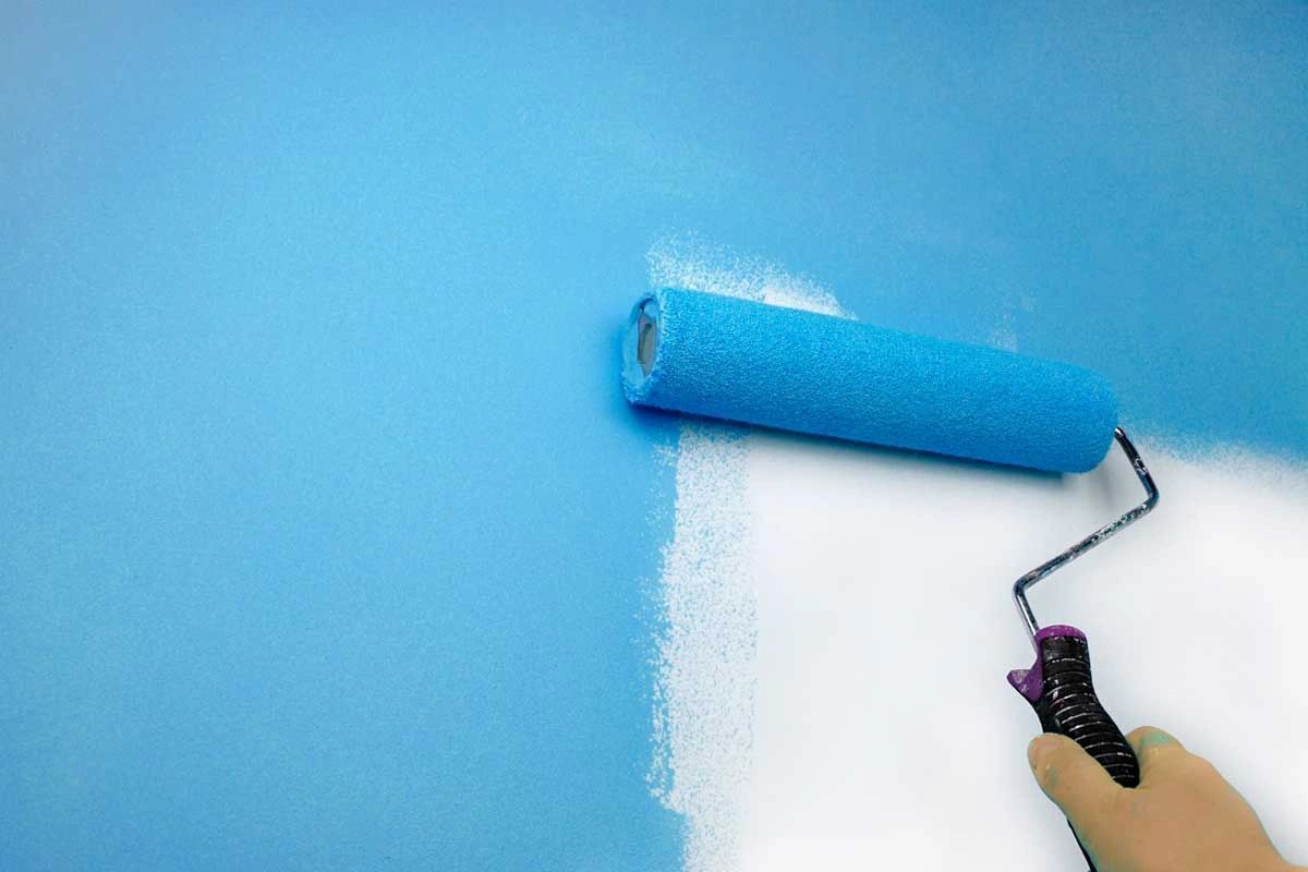 A person is painting a blue wall with a blue paint roller.