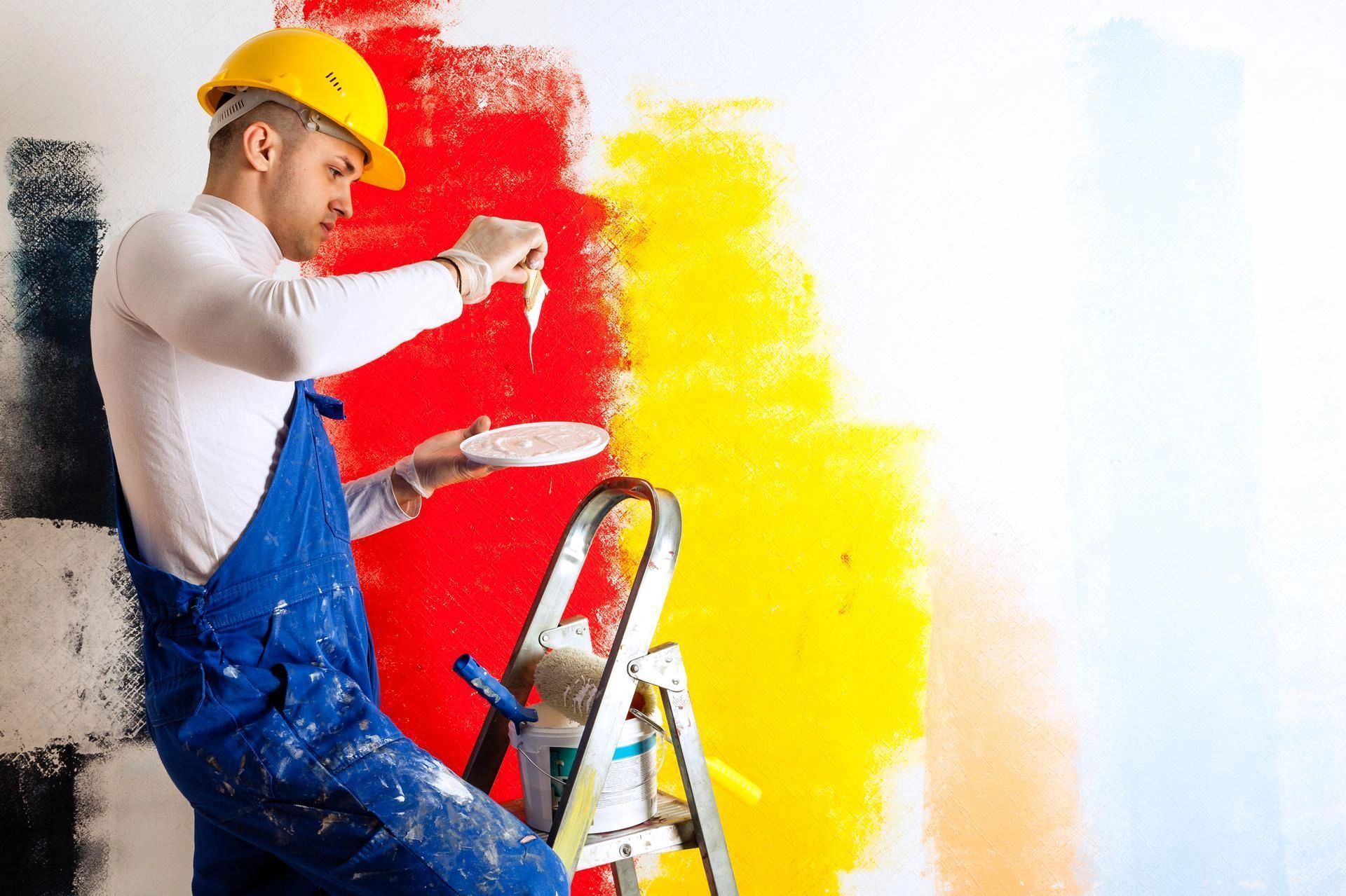 A man is sitting on a ladder painting a wall.