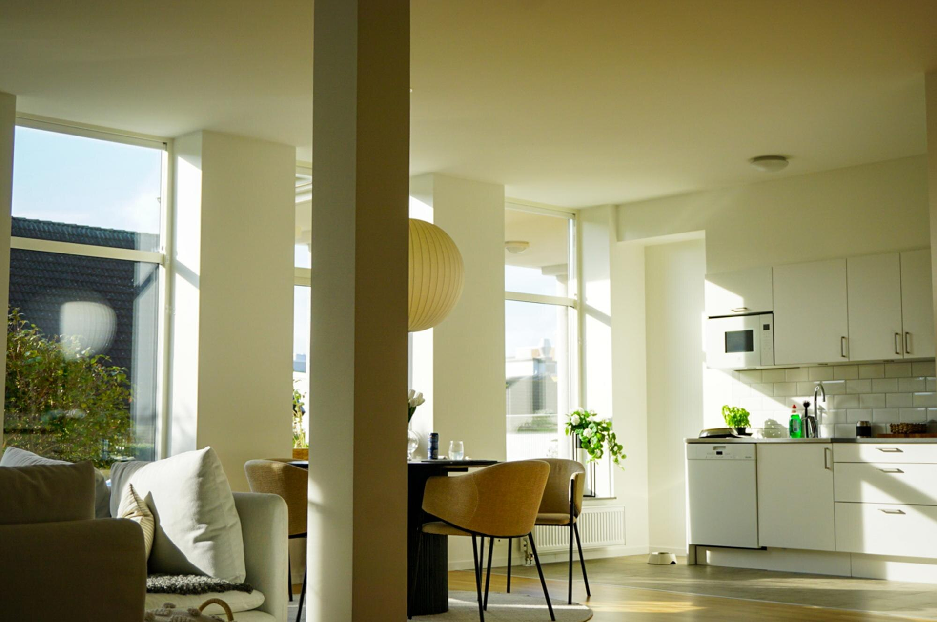 Bright modern open-plan living room and kitchen with sunlight, white walls, and a small dining table
