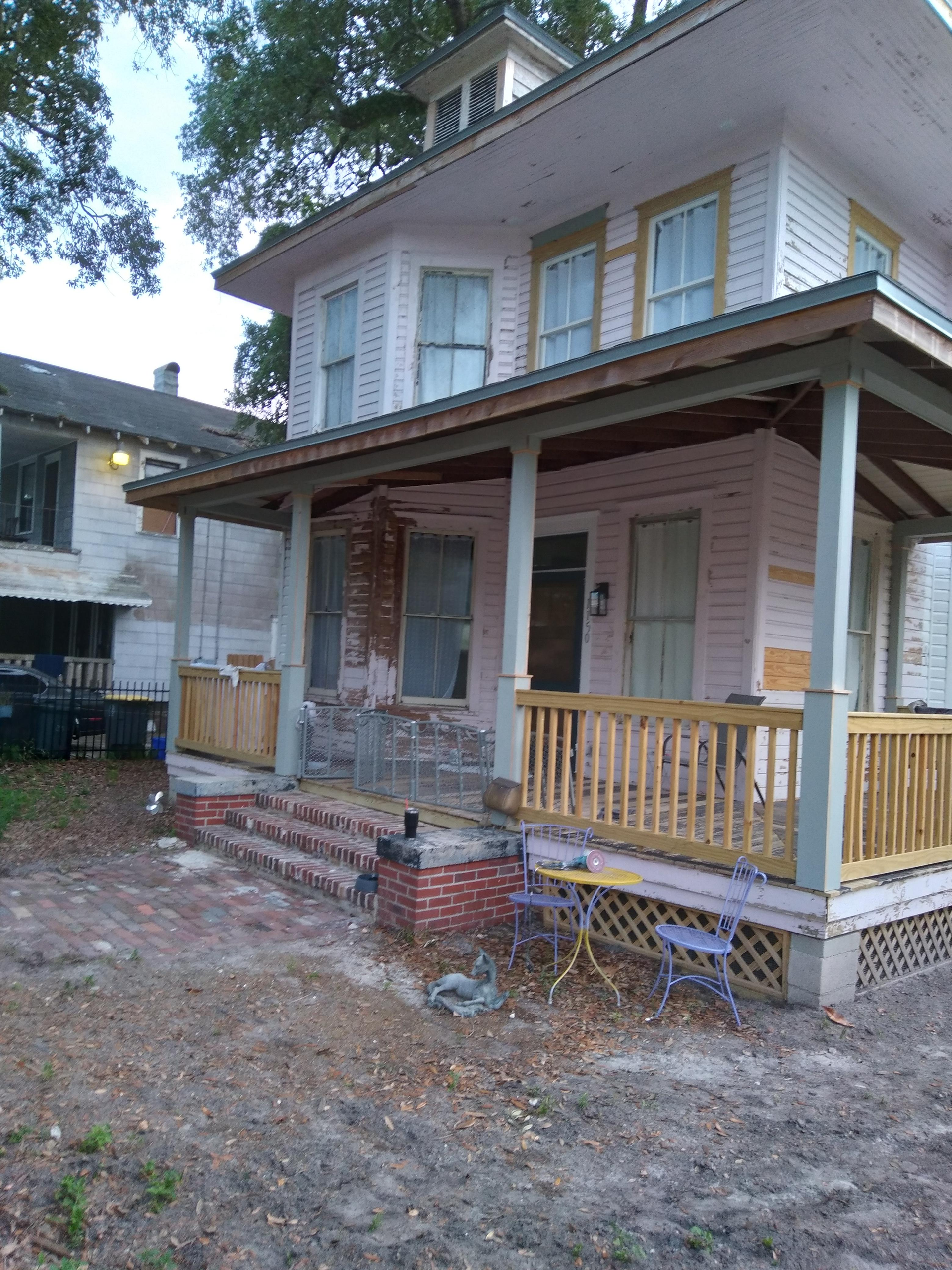 Two-story white house with yellow trim, covered porch, and brick steps in a wooded yard