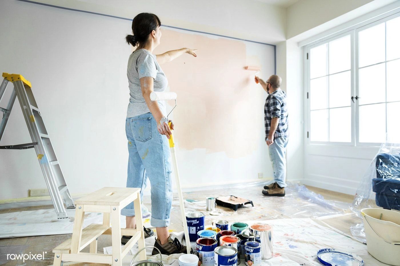 A man and a woman are painting a wall in a room.