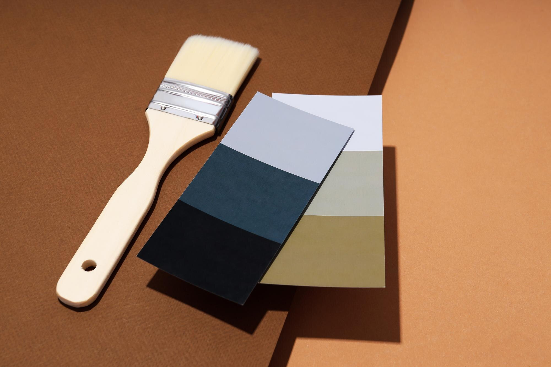 Paint swatches and a paintbrush on a tan surface, showing four neutral color samples.