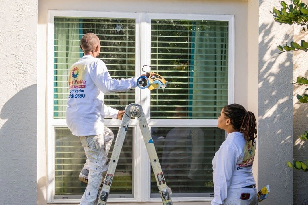 A man and a woman are painting a window on a house.