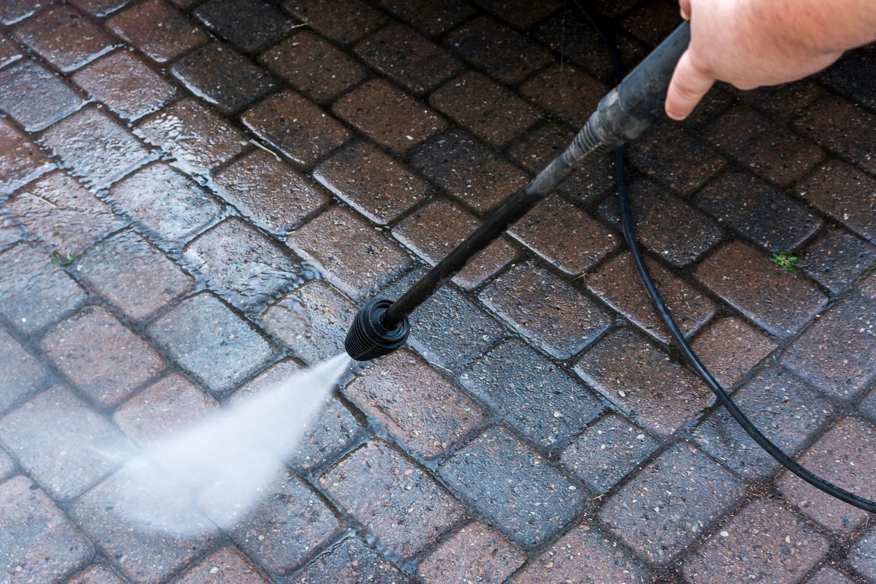 A person is using a high pressure washer to clean a brick floor.