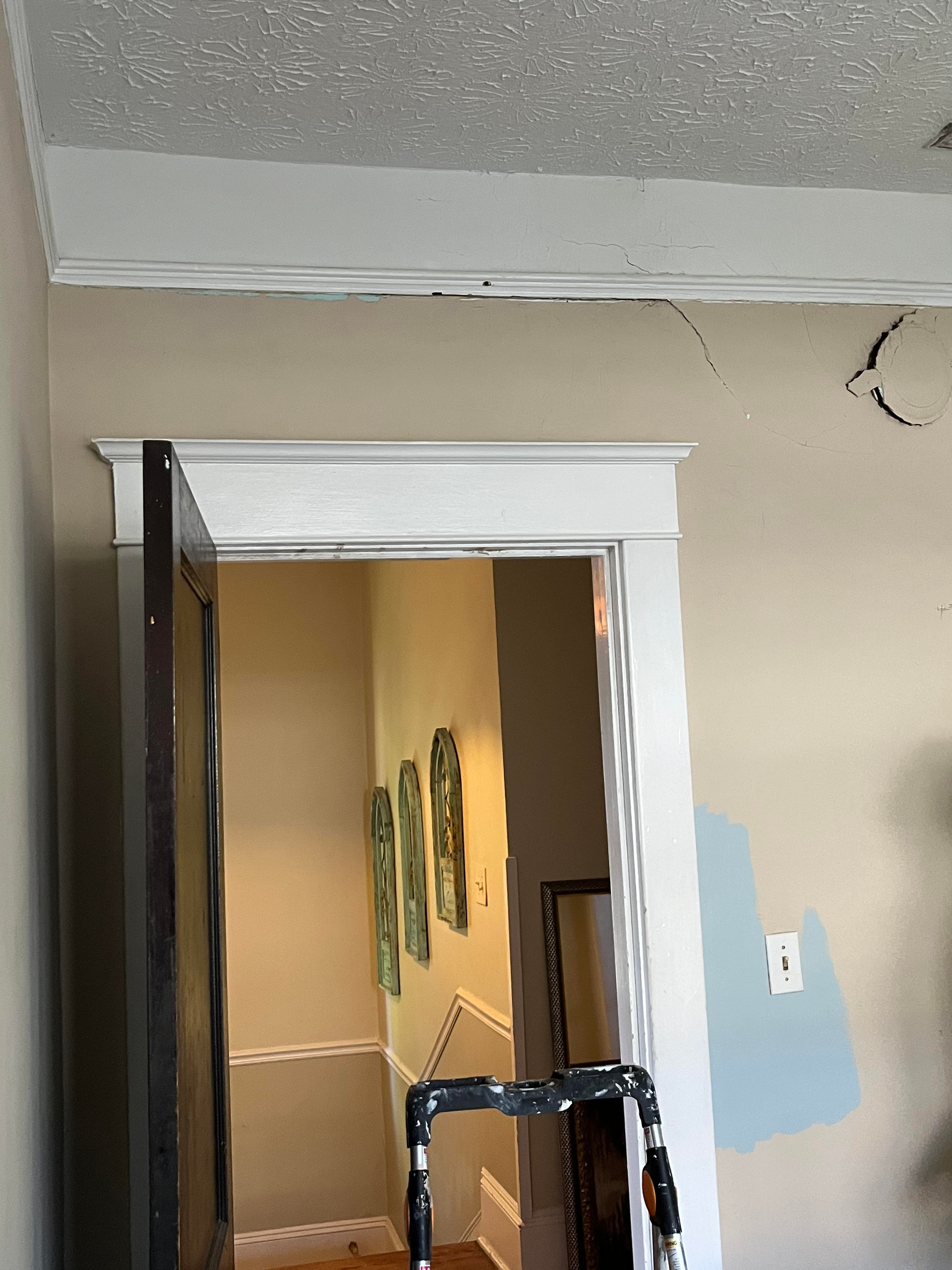 Open doorway with white trim in a beige room; a step stool sits in the opening and a blue paint patch is on the wall