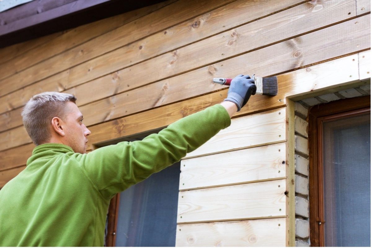 A man is painting a wooden wall with a brush.