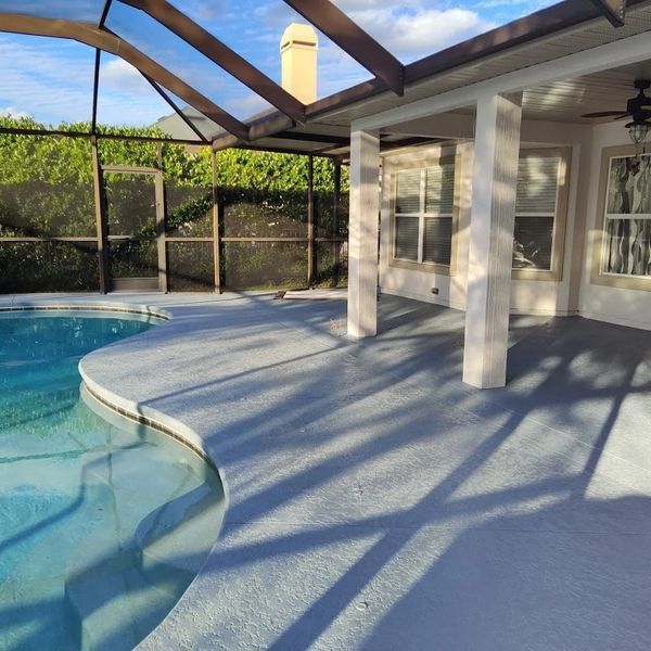 Covered poolside patio with white columns, screened enclosure, and blue pool water at sunset.