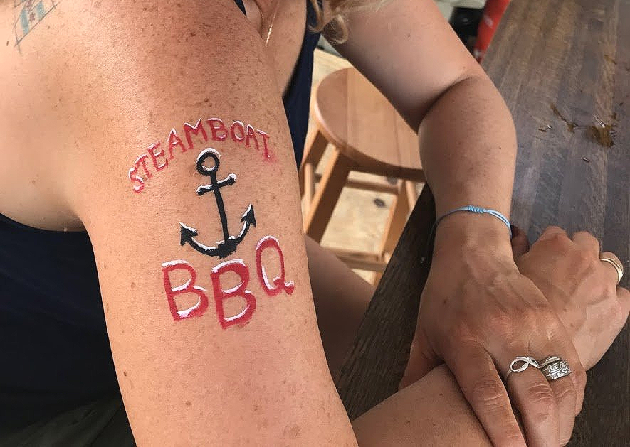 A woman has a tattoo on her arm that says steamboat bbq.
