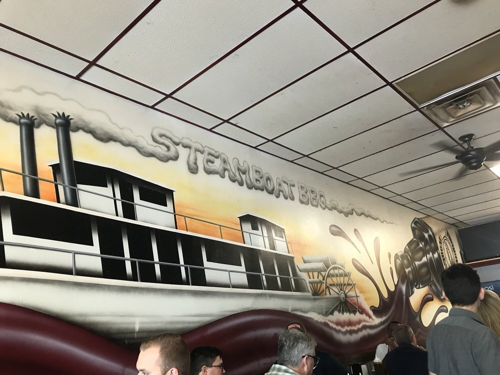 A group of people sitting in a restaurant with a mural on the wall that says steamboat