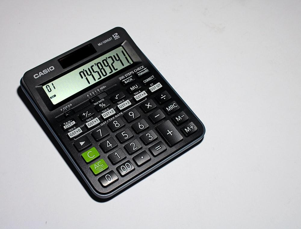 A black casio calculator is sitting on a white surface.