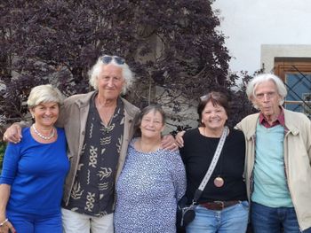 Fünf lächelnde Personen stehen draußen vor einer Mauer mit lila Laubwerk.