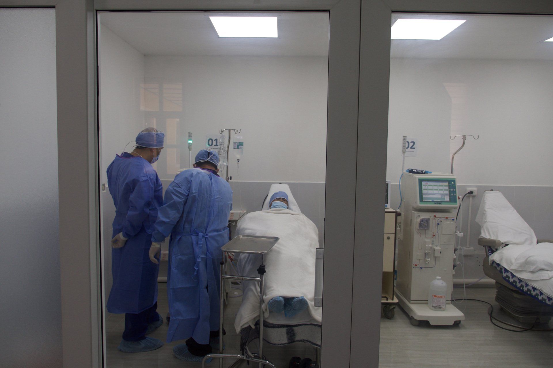 Zwei medizinische Fachkräfte in blauer OP-Kleidung kümmern sich in einem Krankenzimmer um einen Patienten