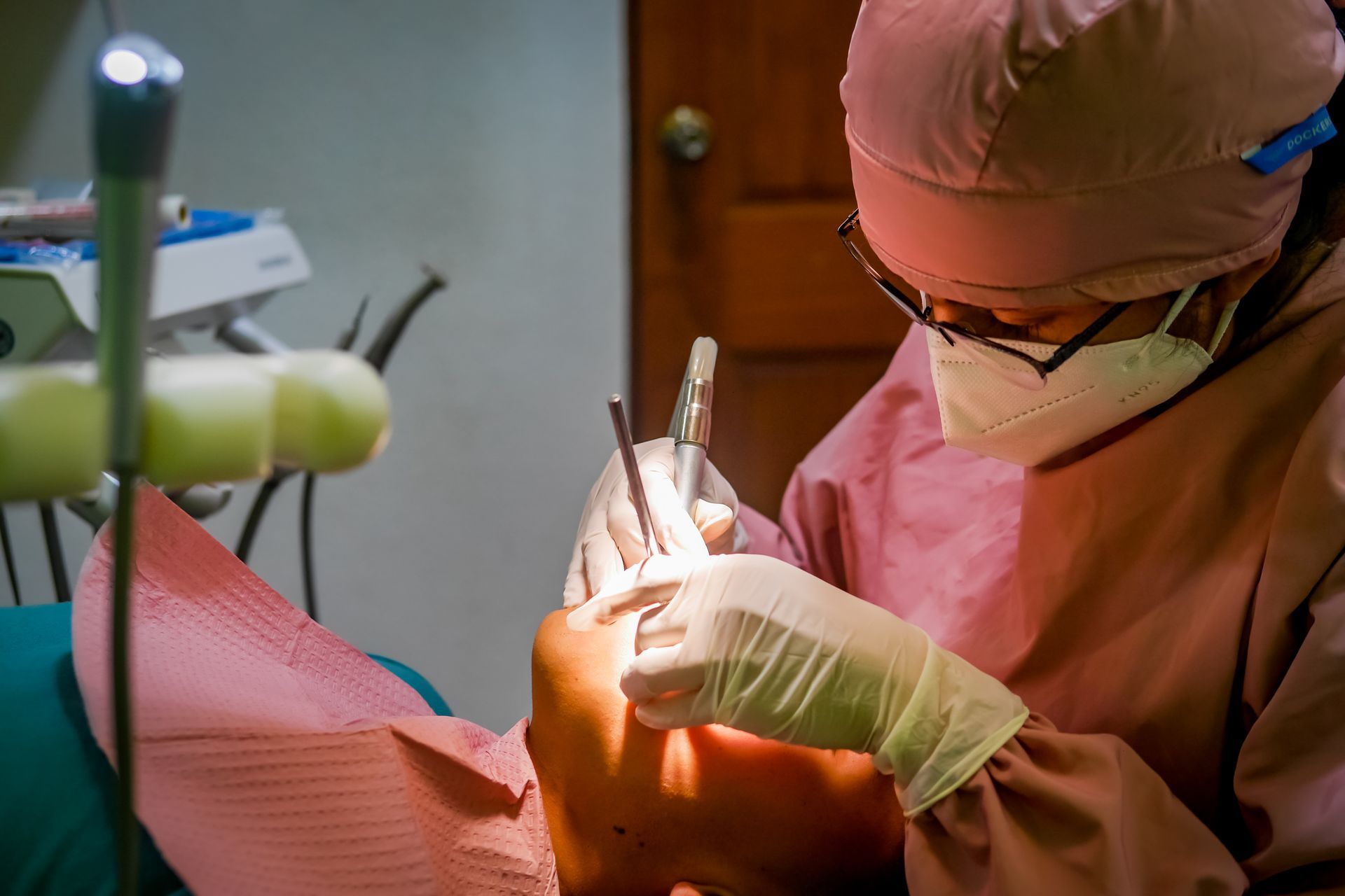 Ein Zahnarzt in Schutzkleidung arbeitet mit zahnärztlichen Instrumenten im Mund eines Patienten.