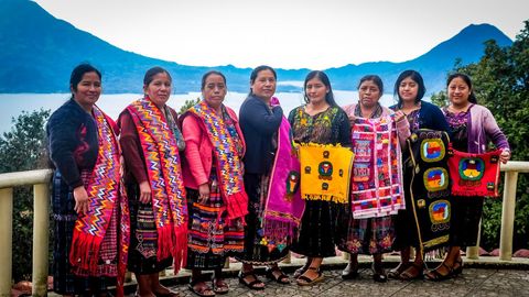 Eine Gruppe von Frauen in traditioneller Webkleidung steht in der Nähe eines Sees und der Berge.