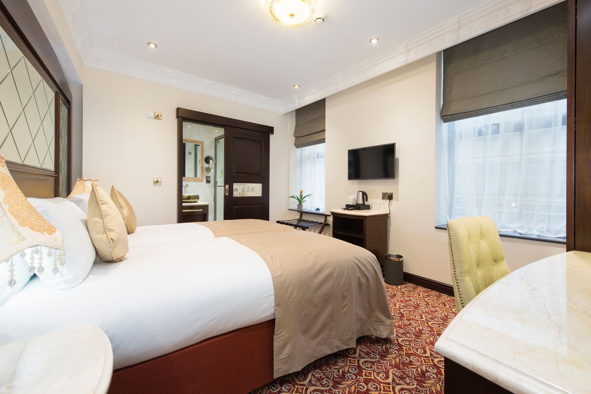 Hotel bedroom with a bed, TV, and en-suite bathroom. Dark wood accents and patterned carpet.