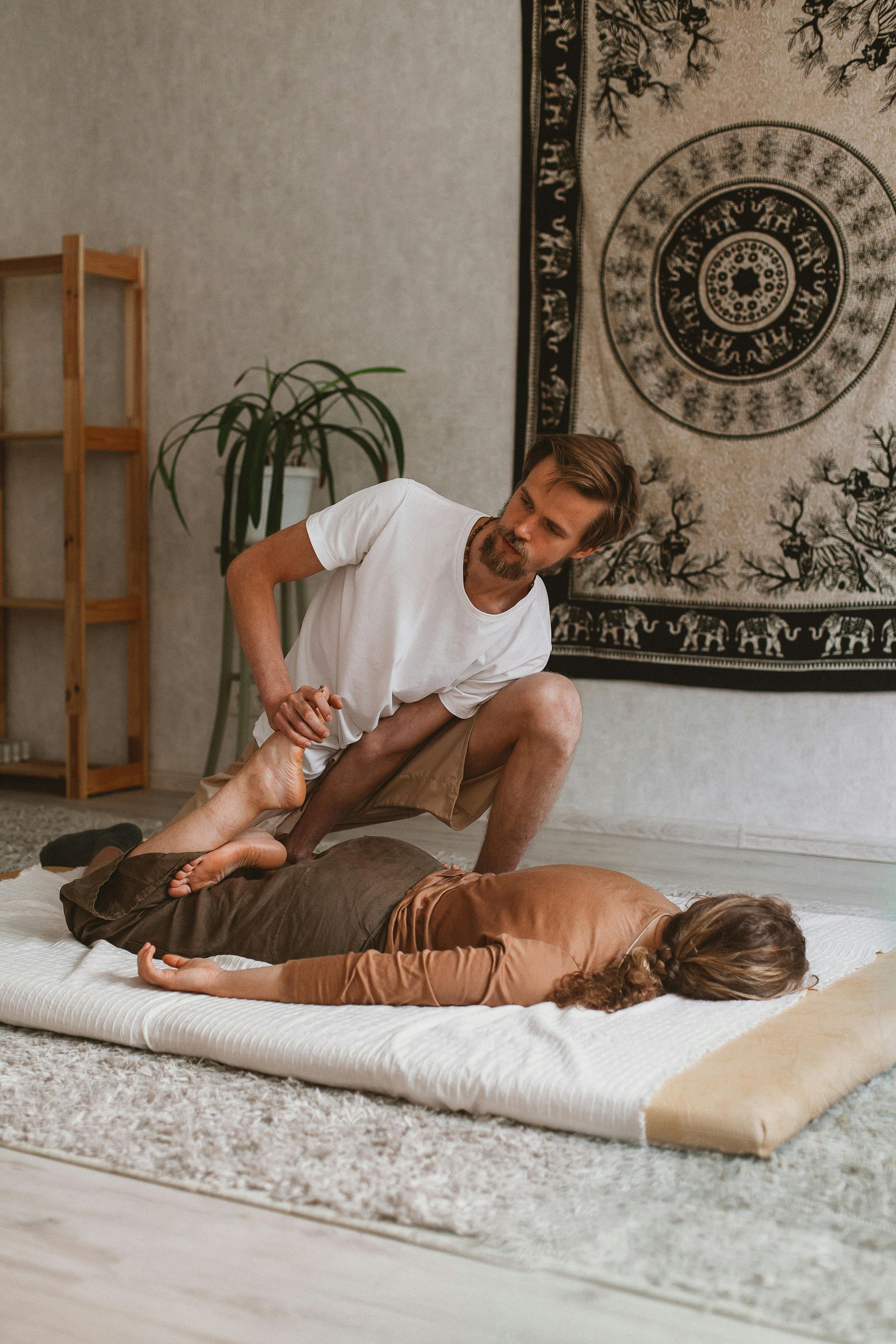 Man performing Thai massage on a person lying on a mat; light, neutral room.